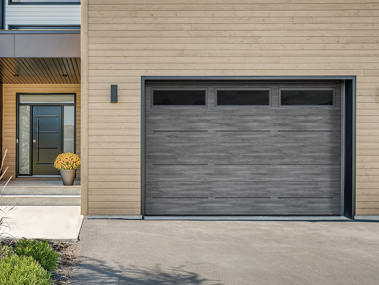 Garaga residential garage door with a Weathered Grey faux-wood finish, the Vogue design and Black Satin glass.