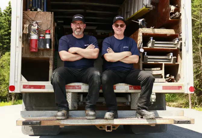 Two technicians sitting in the back of their service truck.
